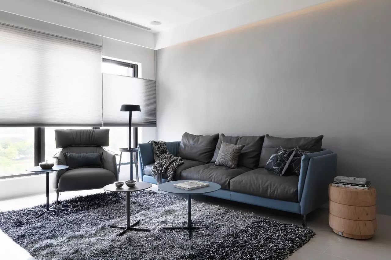 客厅背景墙以灰色为主，搭配灰色皮质沙发和地毯，空间显得通透又安静。
