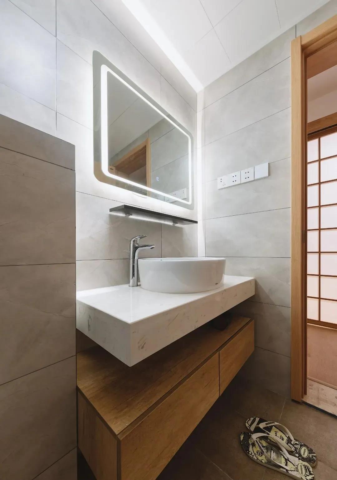 卫生间以灰色和木色打造，洗手池层次分镜，灯光布置巧妙，提升灯光氛围。