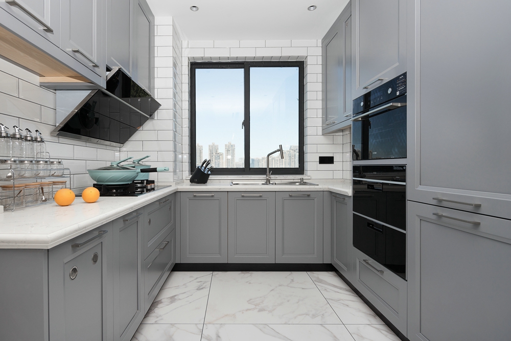 U型厨房设计，冷色调橱柜使厨房空间简洁有序，白色背景墙提升了整洁度。