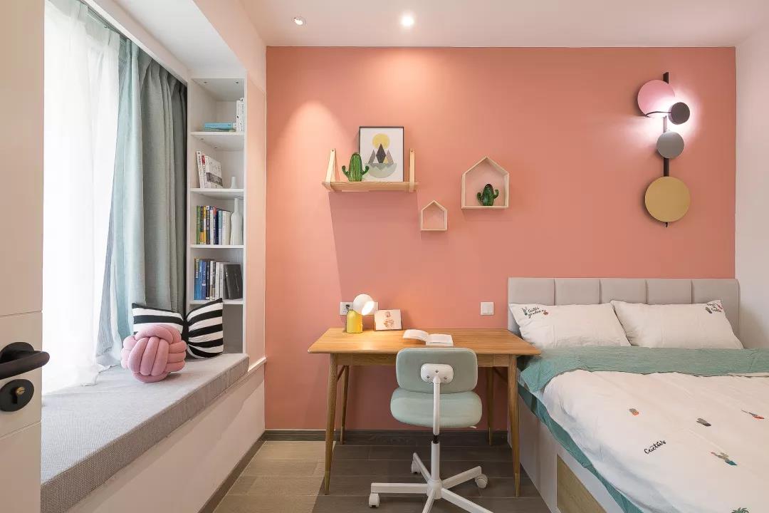 粉橘色背景墙给儿童房增加了童话气息，单人床靠墙摆放，左侧规划了学习区。