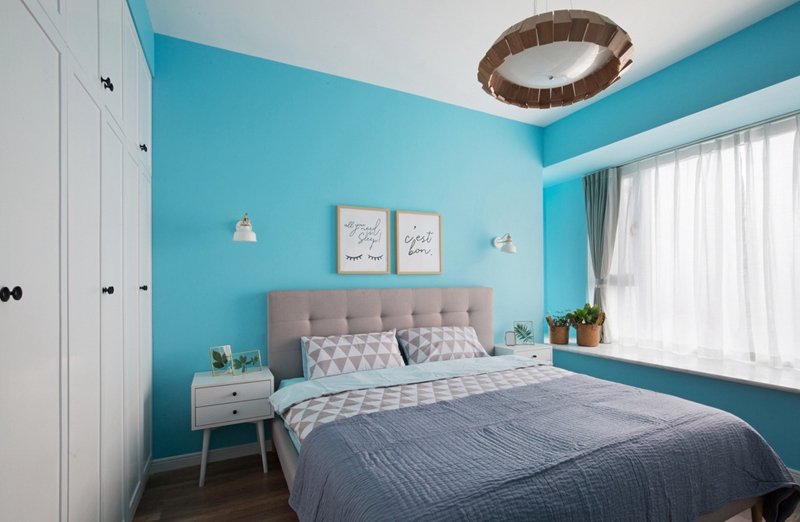 次卧空间以蓝色为背景主题，搭配粉紫色床品，营造出个性温馨的空间氛围。
