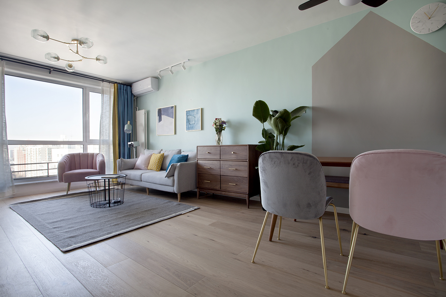 客厅以暖色系为主色调，灰色沙发搭配蓝黄抱枕，再配以粉色座椅，展现出北欧风格的治愈气息。