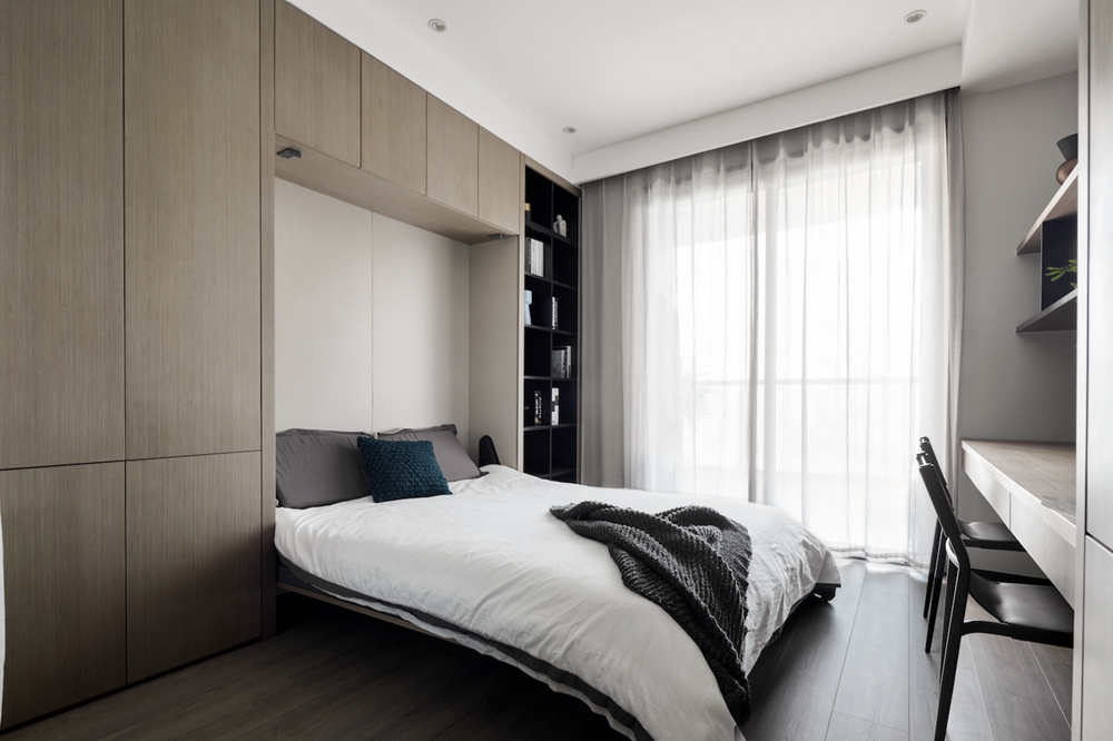 侧卧质朴氛围浓郁，背景墙使用木质柜设计，搭配白色床品与素色窗帘，温馨而舒适。 