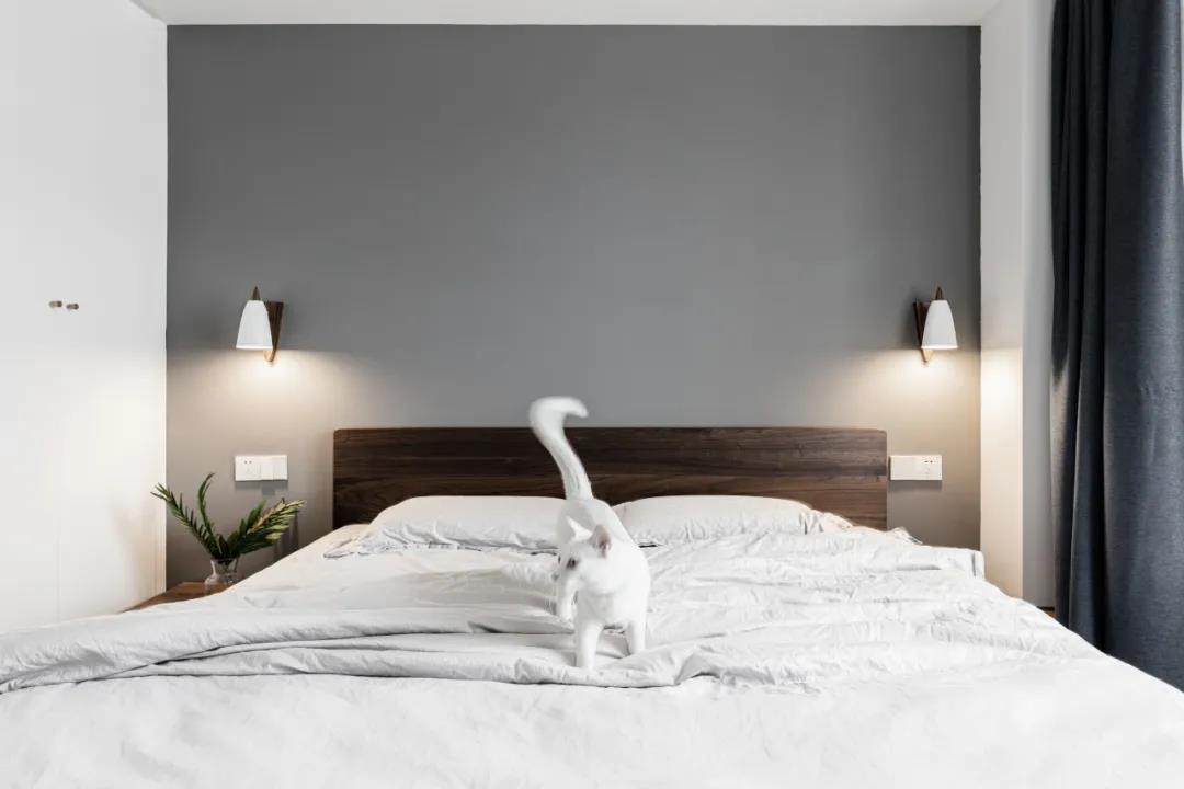 次卧背景是浅灰色，搭配木质床头和白色床品，使空间里充满了素净的生活情趣。