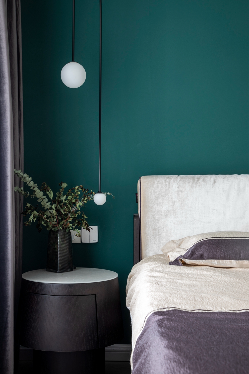 卧室最引人注目的是床头背景墙，墨绿色让整个空间分外静谧，床头垂吊灯提升空间动感。