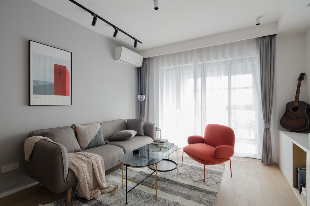 客厅区域以灰色为主，灰色布艺沙发稳重大气，细腿茶几精致感满满，局部橘红点缀，现代感十足。