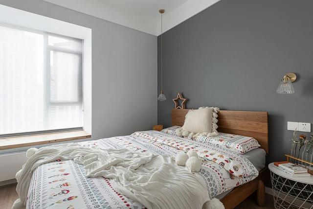 次卧背景墙使用了灰色涂料，床头垂吊灯具洒下柔和的灯光，空间温暖又舒适。