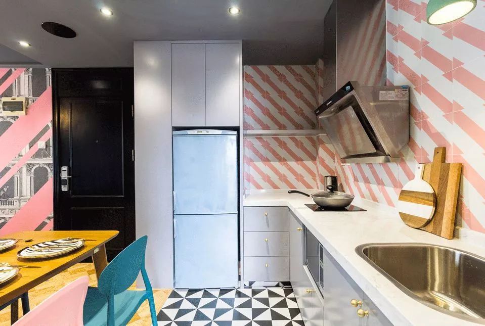 厨房处选择了L型的橱柜布局，把冰箱也嵌入橱柜当中，墙面的粉白色瓷砖和地面的黑白色瓷砖都是几何形状。